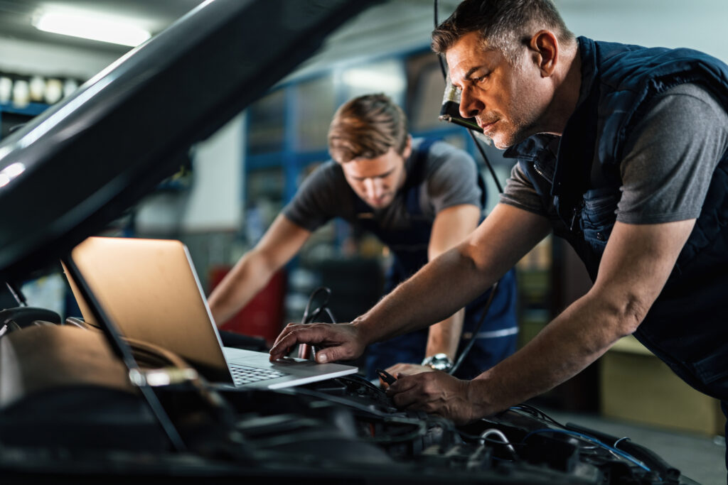 Auto mechanic using laptop while working on car diagnostic with his coworker.